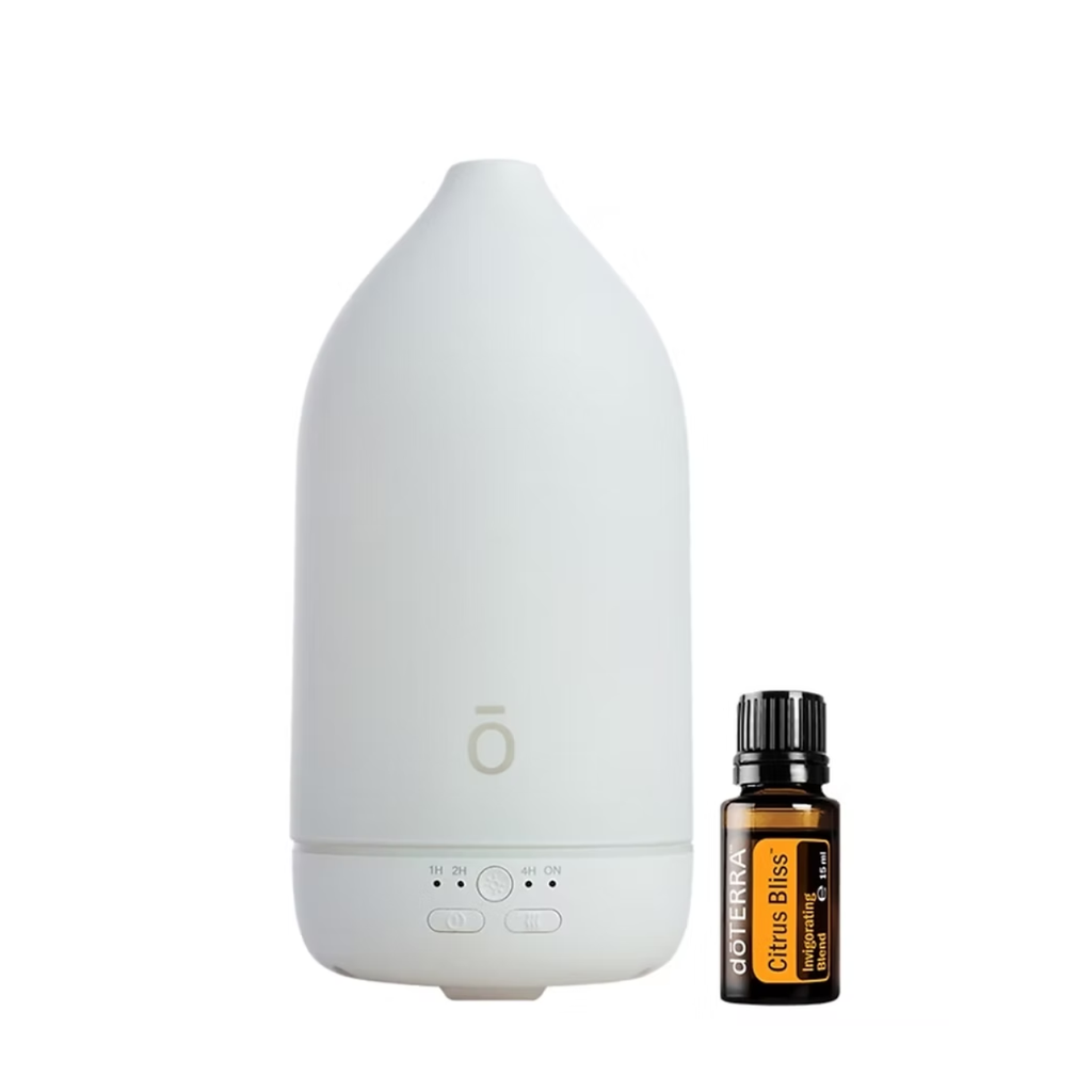 A white essential oil diffuser with a minimalist design stands next to a small amber glass bottle of doTERRA Citrus Bliss essential oil on a solid white background.