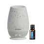 A doTERRA Air diffuser lamp in a speckled off-white ceramic style next to a small amber glass essential oil bottle with a black cap and blue label, on a plain white background.