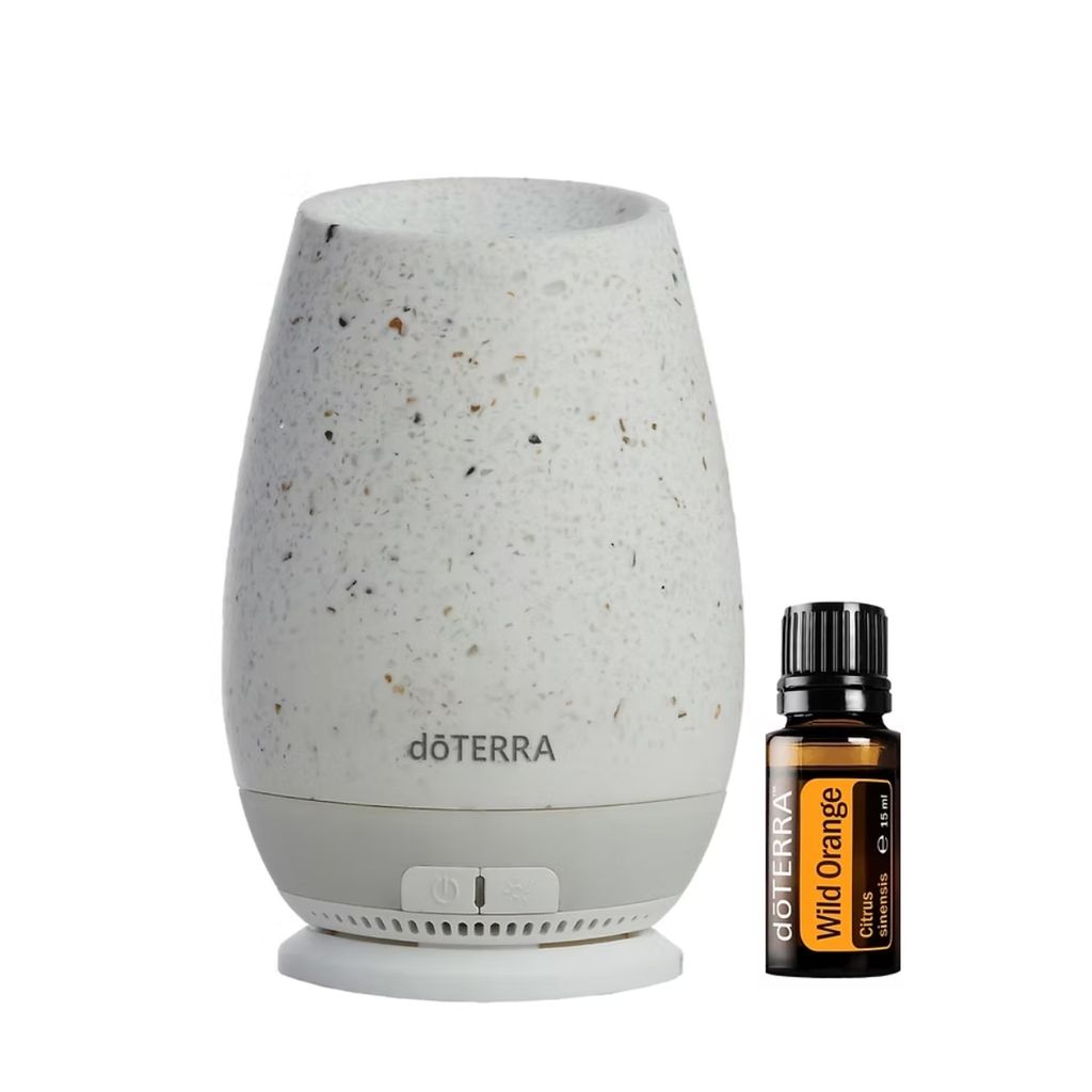 A döTERRA diffuser lamp in a speckled off-white ceramic finish stands next to a small amber glass bottle of döTERRA Wild Orange citrus oil on a clean white background.