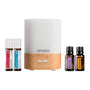 A doTERRA essential oil diffuser with a white and light wood base, shown with four doTERRA essential oil bottles on a plain white background.